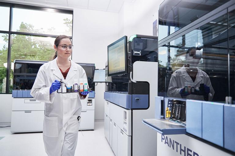 Female lab technician carrying a tray of specimens to insert into medical system