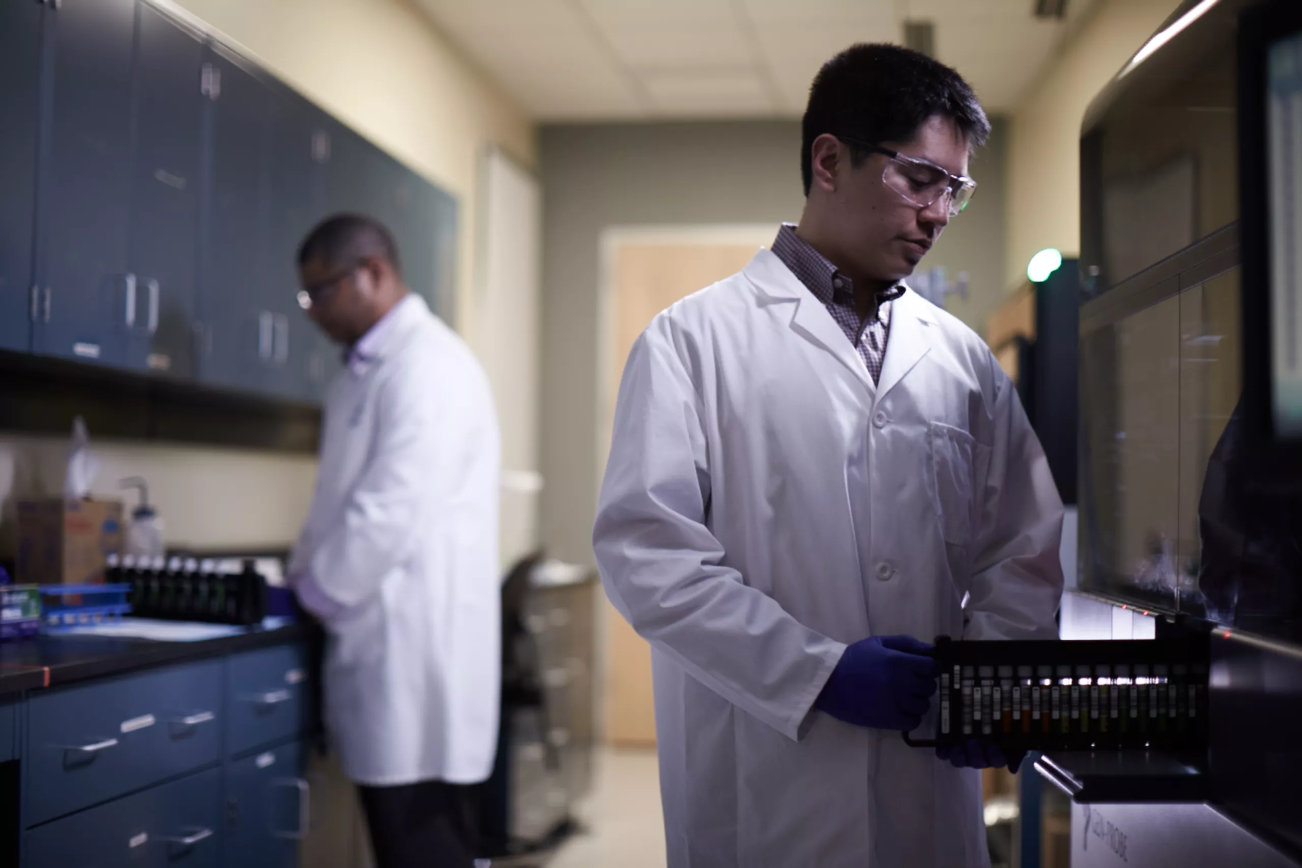 Male lab technician pushing tray of vials into medical system